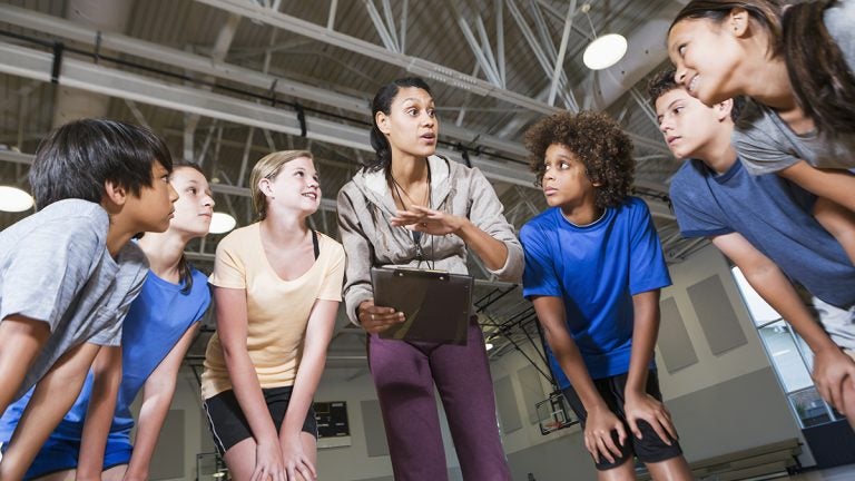 Coach talking to group of kids in gymnasium