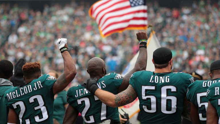 Rodney McLeod and Malcolm Jenkins raise their fists in protest while Chris Long of the Philidelphia Eagles puts arms around teammates in support