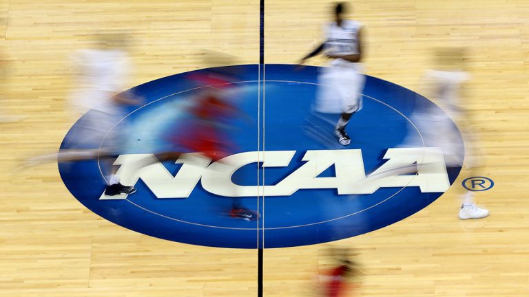 Basketball court with NCAA logo on it and basketball players running by