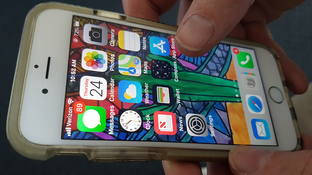 An unlocked iPhone showing home screen apps with someone's finger hovering over the app store