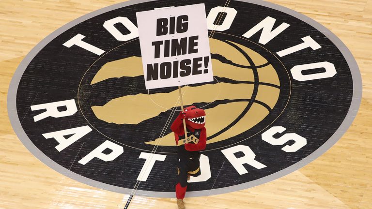 Raptor the mascot of the Toronto Raptors holds a sign at center court imploring fans to make noise over the team logo.