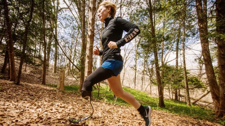 Person with a prosthetic leg running up an inclined hill with leaves on it