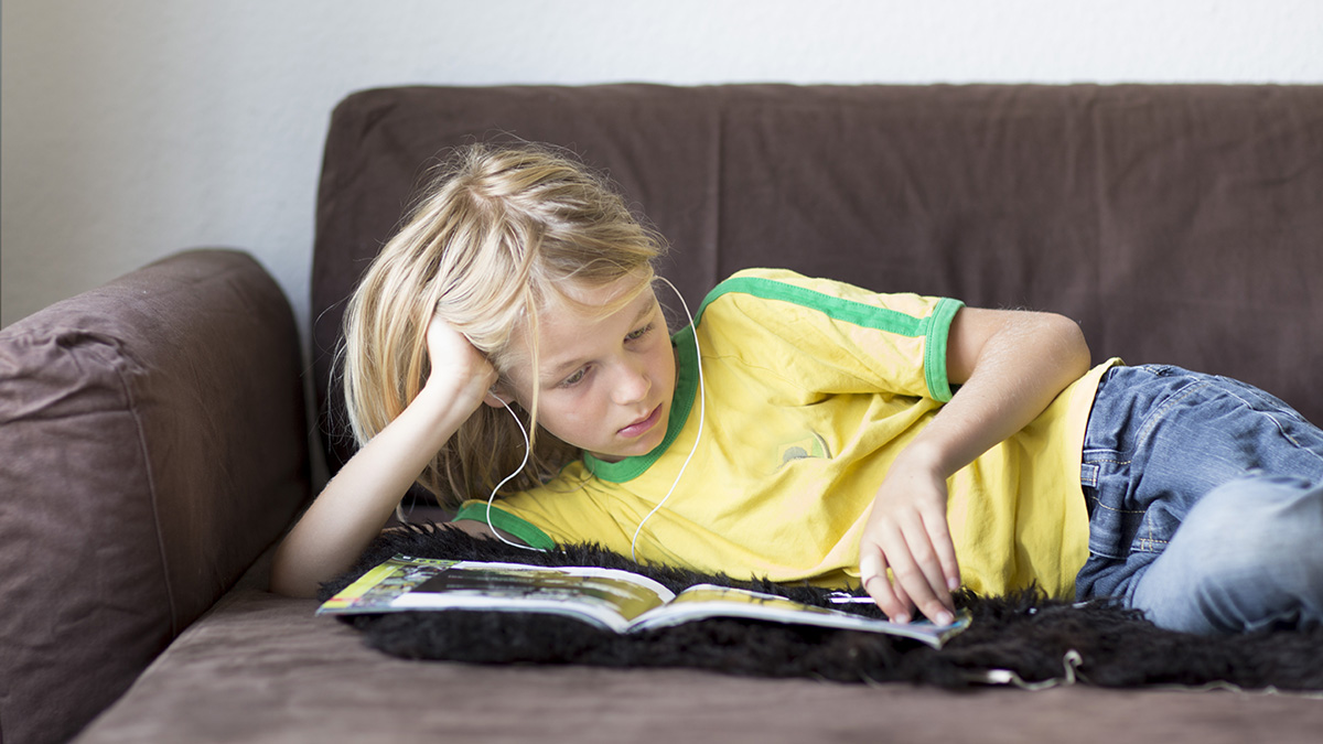 Child lays inactive while listening to music and reading a book