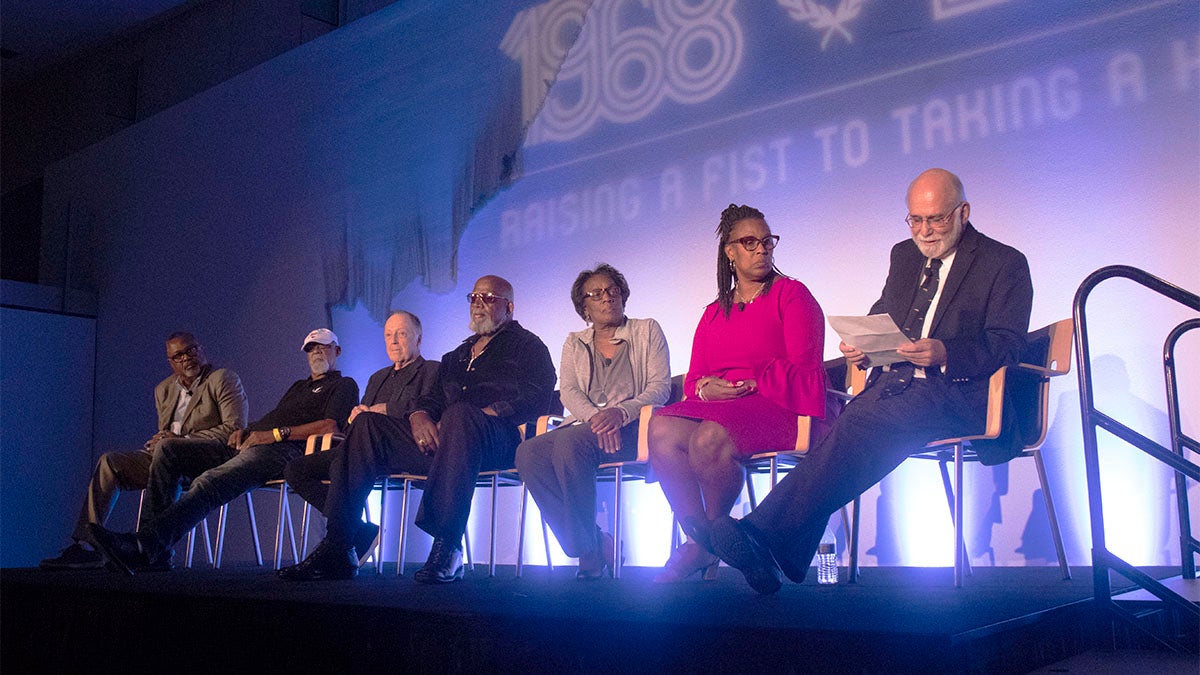 Kenneth Shropshire, John Carlos, Lance Wyman, Harry Edwards, Wyomia Tyus, Gina Hemphill-Strachan, and Paul Hoffman discuss the athlete protests at the 1968 Summer Olympics