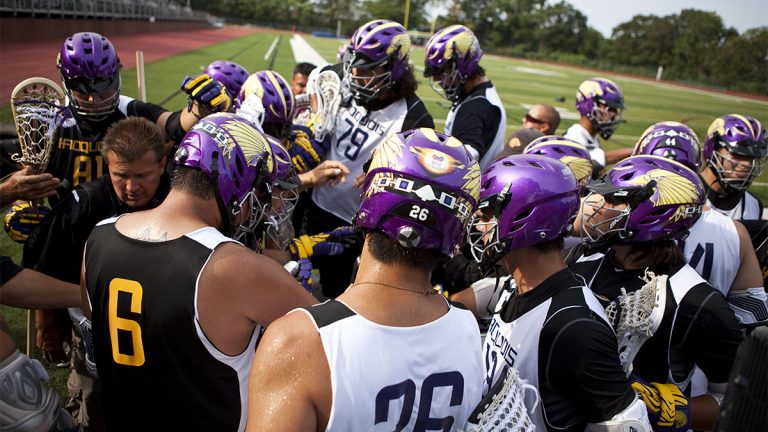 Lacrosse players with purple helmets in a huddle