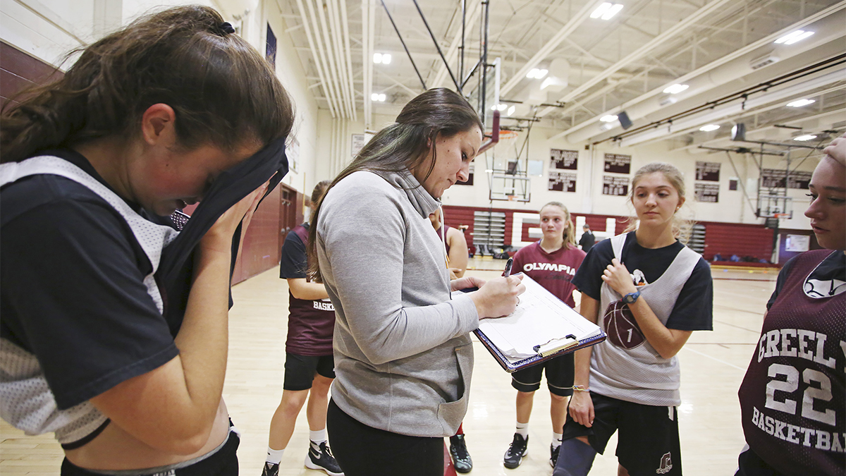 Youth coach writing in playbook for girls basketball team.