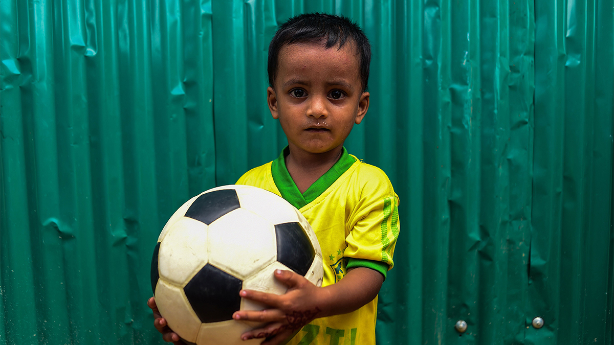 A child holding a soccer ball at a refugee camp.