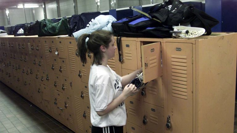 High school girl grabbing shoes from her locker in girls' locker room