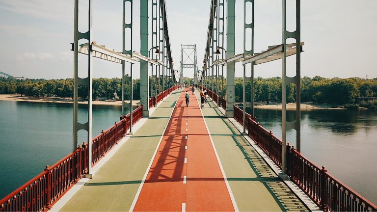 Pedestrians on a bridge over water that features a painted track through the middle of the pathway.