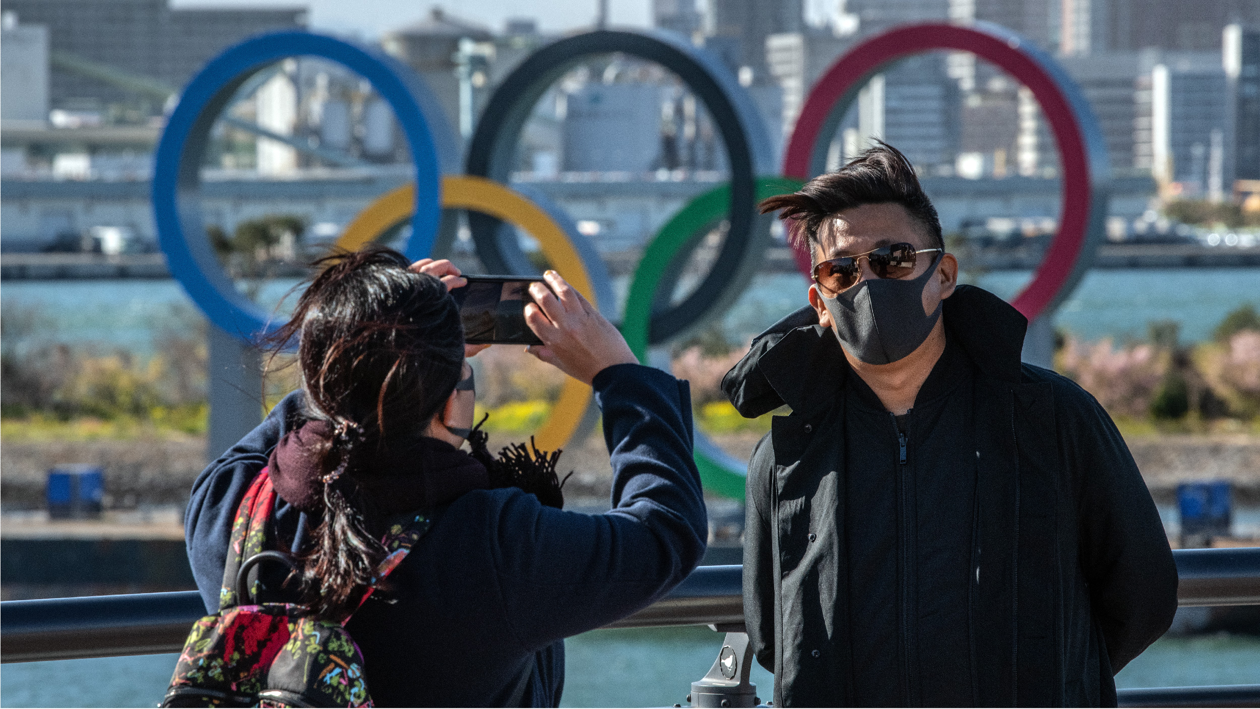 TOKYO, JAPAN - MARCH 05: A man wearing a face mask has his photograph taken in front of the Olympic Rings in Odaiba on March 5, 2020 in Tokyo, Japan. An increasing number of events and sporting fixtures are being cancelled or postponed around Japan while some businesses are closing or asking their employees or work from home as Covid-19 cases continue to grow and concerns mount over the possibility that the epidemic will force the postponement or even cancellation of the Tokyo Olympics. (Photo by Carl Court/Getty Images)