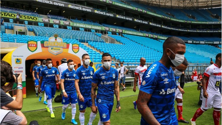 PORTO ALEGRE, BRAZIL - MARCH 15: Players of Gremio enter the field wearing masks before the match between Gremio and Sao Luiz as part of the Rio Grande do Sul State Championship 2020, to be played behind closed doors. (Photo by Lucas Uebel/Getty Images)