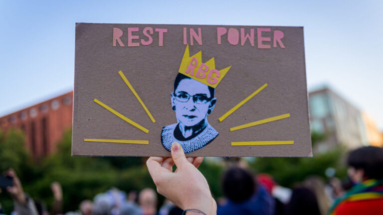 A Ruth Bader Ginsburg poster saying "Rest in Power RBG" being held by a hand.