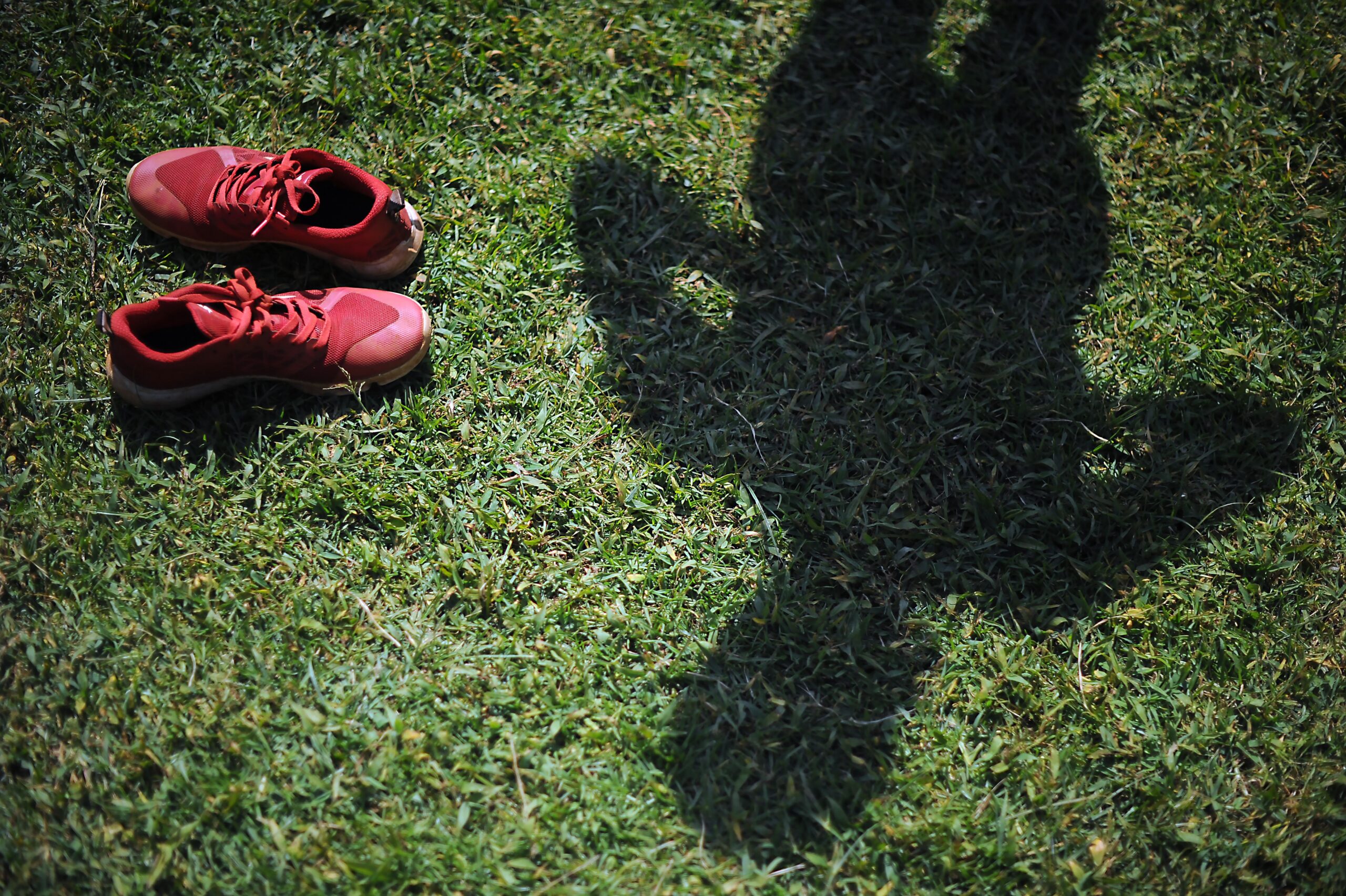 An athlete's shadow faces grass with a pair of red sneakers on the side