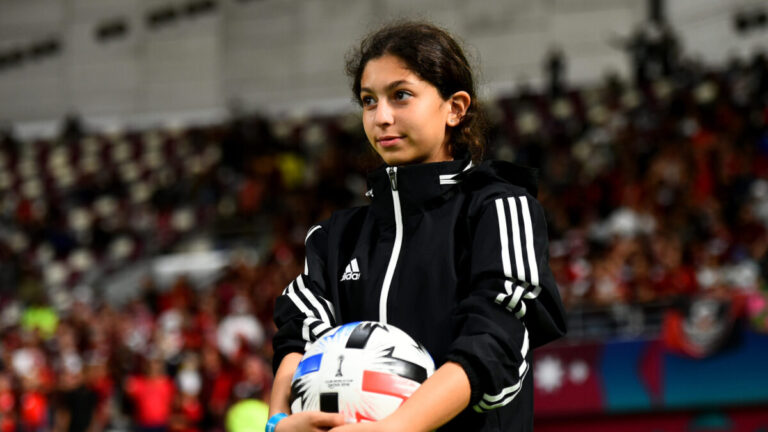 A young girl watches a soccer game with a ball in hand