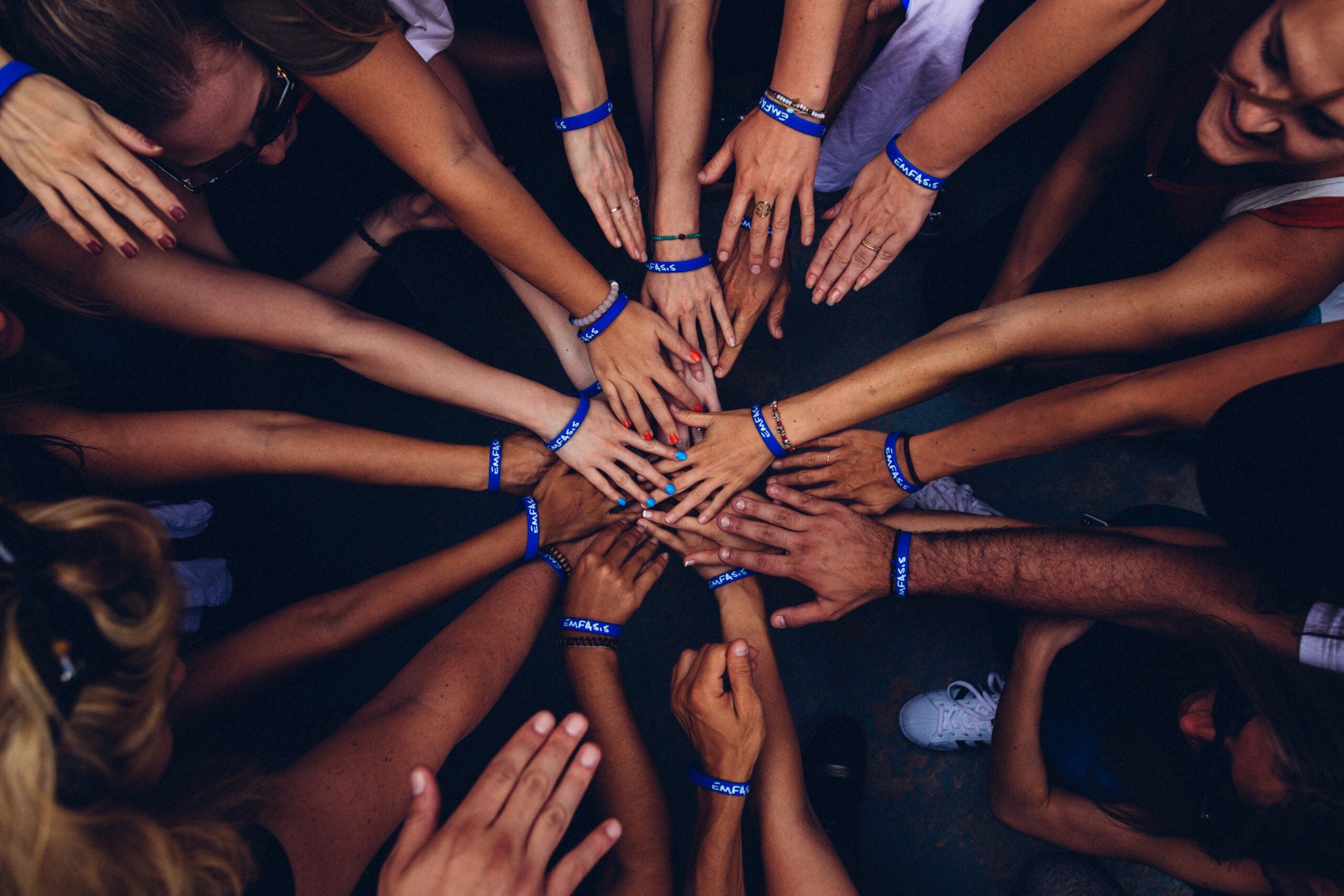 A top-down view of several women and men putting their hands in the center as if it is right before a team chant.