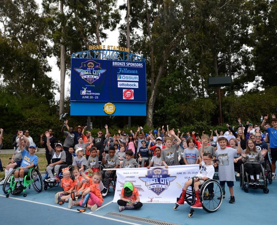 A large group photo of youth adaptive athletes on a court; many of them are waving their hands in the air. (Photo courtesy of Angel City Sports)