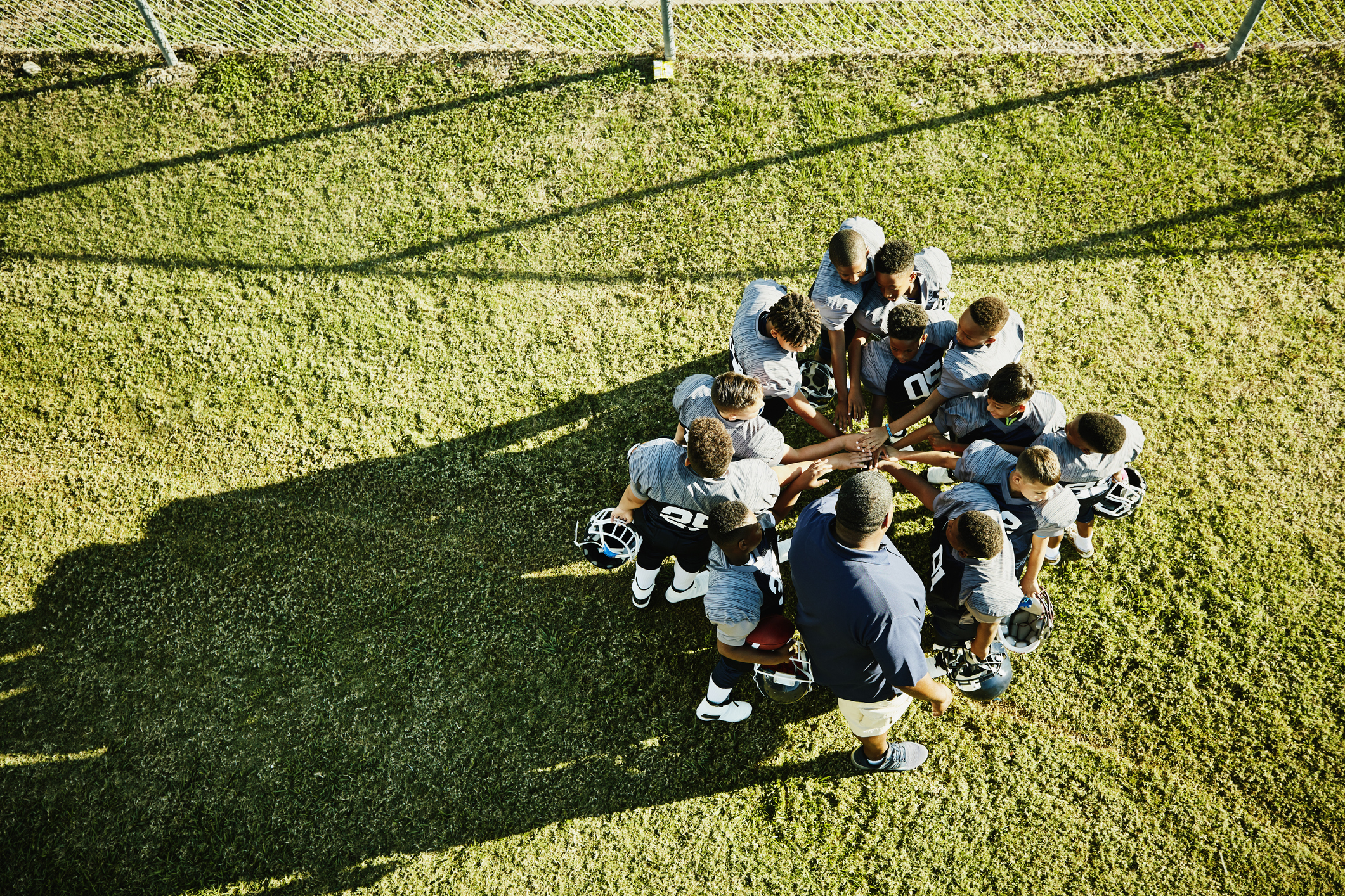 Overhead view of coach and football team gathered in circle with hand together before football game